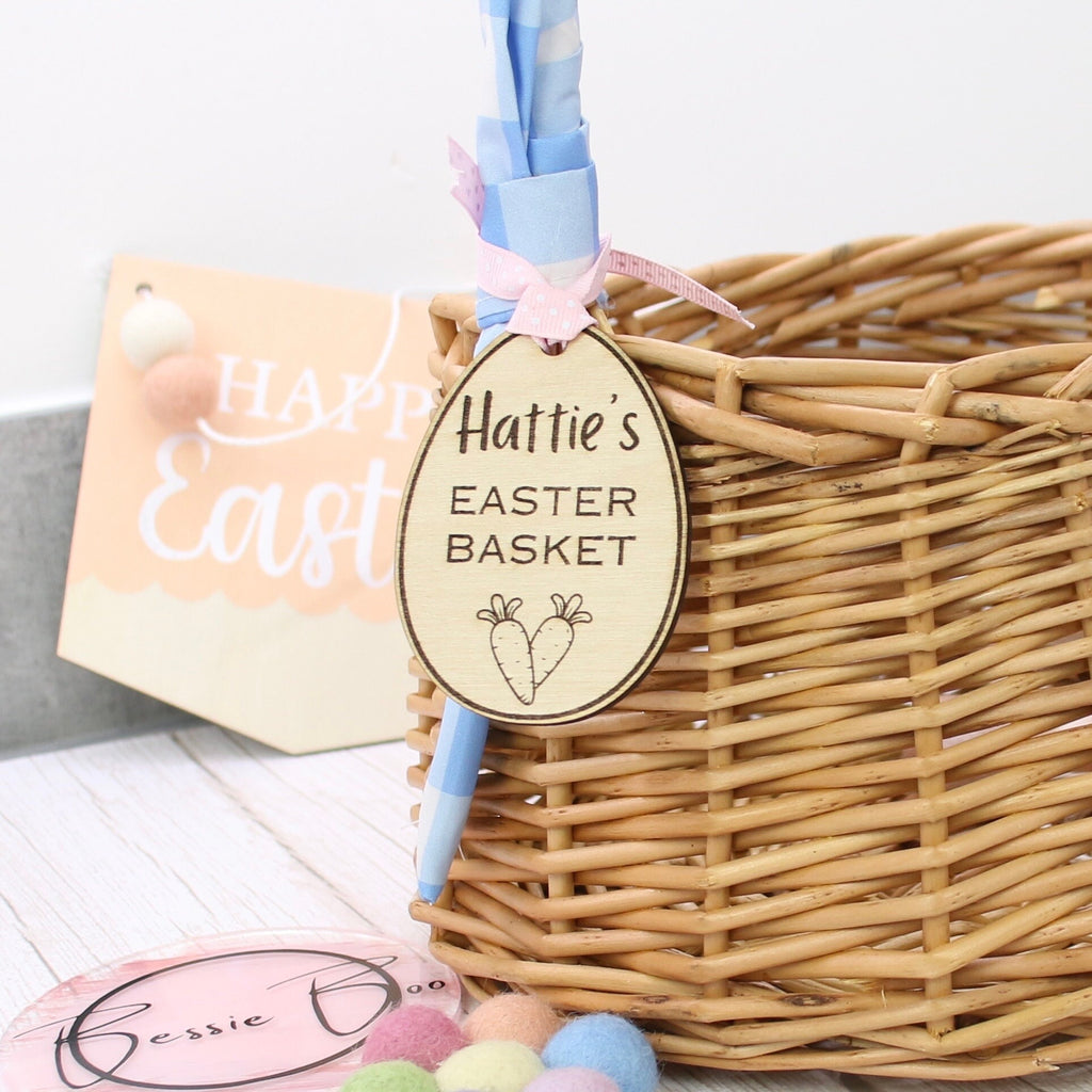 8cm Easter basket wooden tag in the shape of Easter Egg cut from 3mm Plywood. Item includes personalised text, e.g. name of a child. The tag is shown attached to a wicker basket, it includes 2 small carrots and text says: Hattie&#39;s Easter Basket